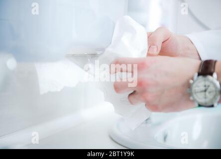 Close Up Of Caucasian Male Drying Out Hands Using Disposable Paper Towels In Bathroom. Stock Photo