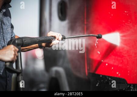 Close Up Of Man Spraying Exterior Of Red Semi Truck Using Self Service Equipment At Car Wash. Stock Photo