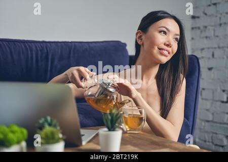 Joyful young woman drinking tea and using laptop Stock Photo