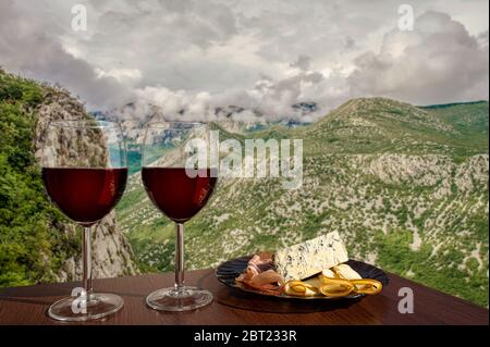 Two glasses of wine with charcuterie assortment on view of mountains with clouds in Croatia. Dinner in cafe or restaurant with mountains view. Stock Photo