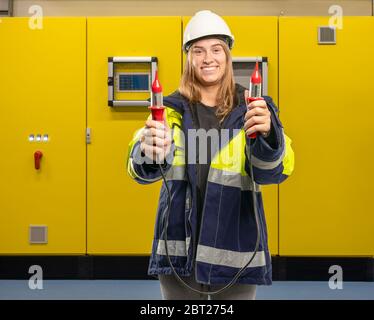 a female electrician in front of a switch cabinet holds up a measuring device Stock Photo