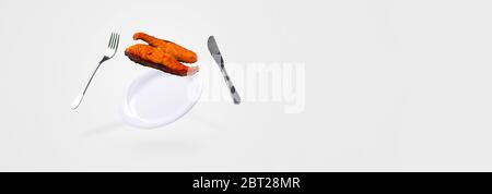 grilled salmon fish falling on the levitating plate, fork and knife. conceptual food background Stock Photo