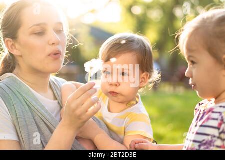 Motherhood, care, infants, summer, childhood and large families concept - Young big mom with newborn baby in sling and two small children of same age Stock Photo