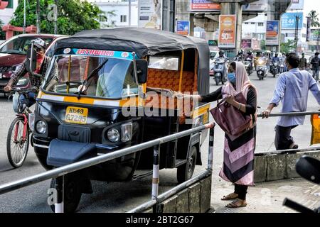 Kochi, India - May 2020: Woman wearing a face mask paying a tuk tuk driver with face mask during confinement for the COVID-19 pandemic on May 22, 2020 Stock Photo