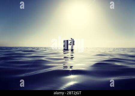 Businessman Standing in the Ocean Searching Through a Filing Cabinet Stock Photo