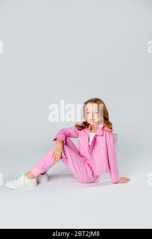 girl in a pink tracksuit and sneakers sits on a light gray background ...