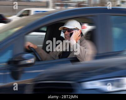 Careless male driver with sunglasses and cap using mobile phone while driving in heavy traffic. Careless or reckless driving is a traffic violation. P Stock Photo