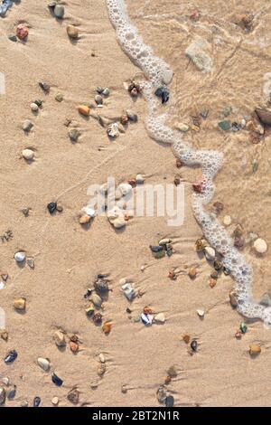 Beach sand top view background with small wave, stones and shells Stock Photo