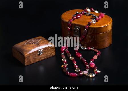 Two Old wooden jewelry caskets and a glass bead necklace isolated on black background. Wooden boxes for different decorations or small trifles. Stock Photo