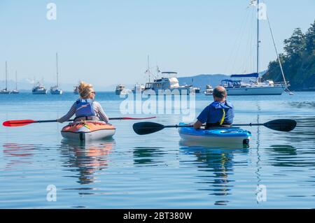 A senior man and  woman in colorful sea kayaks paddling together with large yachts in the background Stock Photo