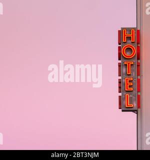 Neon hotel sign on the building corner with pink sunset sky at background. Stock Photo