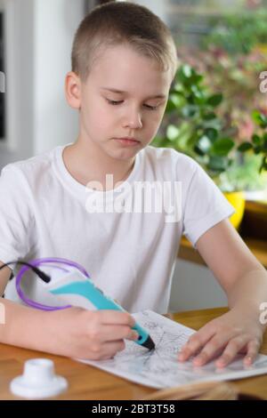 Child using 3D pen. Boy draws on stencil by colored ABS plastic at home. Creative hobby at home, technology, leisure, education concept. Selective foc Stock Photo