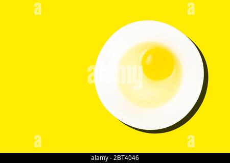 Raw egg in bowl with dark shadow isolated on yellow background. Healthy food and cooking at home concept. Stock Photo