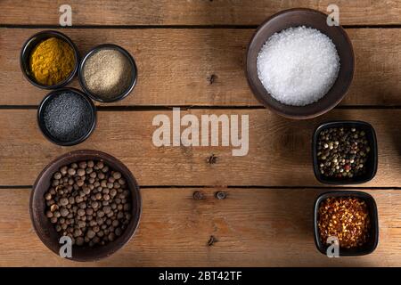 Mix of peppers, white pepper, red dry chillies, puppy seeds, salt, bahari and curry all in different shape of bowls on a wooden surface Stock Photo