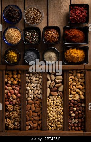 Mix of spices in different shape of bowls and mix of nuts in a wooden box on a wooden surface Stock Photo