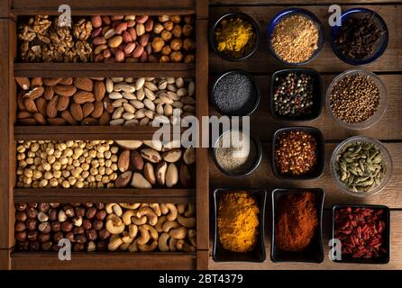 Spices in different shape of bowls and mix of nuts in a wooden box on a wooden surface Stock Photo