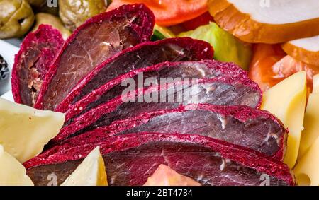 Close-up of basturma sliced into pieces. Restaurant dish on a wooden background with cheese, vegetables. Cured meat Stock Photo