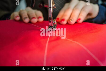 A seamstress, red fabric, women's hands, Hands guiding the cloth in a sewing machine Stock Photo