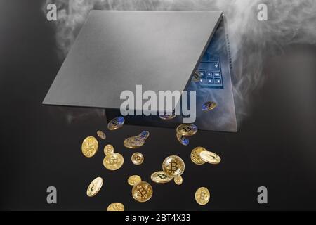 Concept of mining and generating cryptocurrency, falling Bitcoins generated from steaming laptop on plain dark background Stock Photo