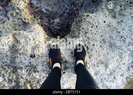 Overhead view of a woman in a wetsuit standing on rocks, Bugibba, Malta Stock Photo