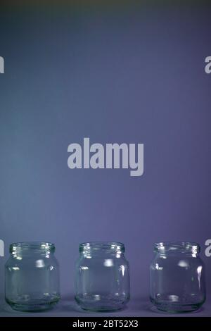 A horizontal row of three transparent jars on a purple vertical background in the shade. Stock Photo