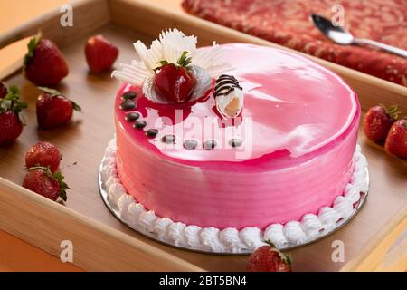Strawberry cheese cake with glazed strawberry topping, chocolate chips on pink colored round cake Stock Photo