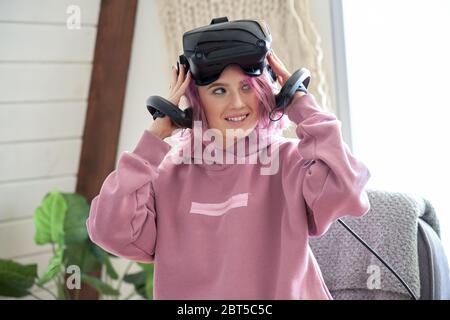 Teen girl pink hair wear vr headset hold controllers experience virtual reality. Stock Photo