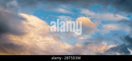 Beautiful colorful panoramic view of summer golden fluffy clouds illuminated by disappearing rays at sunset, dramatic dark thunderclouds in blue sky Stock Photo
