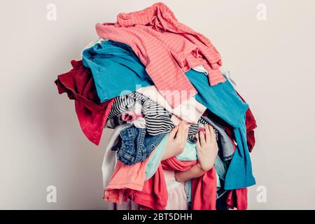 Mommy little helper. Cute Caucasian girl sorting clothes. Adorable funny child arranging organazing clothing. Kid holding messy stack pile of clothes Stock Photo