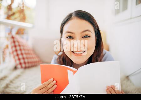 beautiful young woman relaxing and laying down on an exterior bed on a home terrace garden and reading a magazines while on holiday Stock Photo