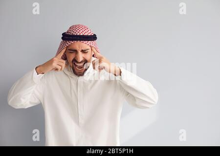 Arabic man shouting holding hands to head on a gray background. Stock Photo