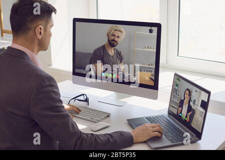 Side view of adult man in suit using computer and laptop to talk with male and female employees while working remotely from home Stock Photo