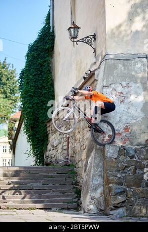 Side view of a strong guy on a black bike doing a dangerous stunt. Sport teacher showing new movement on bicycle. Persistent guy perfecting his sports skills. Concept of dangerous sport. Stock Photo