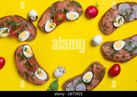 Six bread with salmon sandwiched, quail eggs and vegetables around. on yellow paper, top view. Yellow paper Stock Photo
