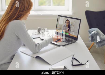 Young woman with ginger hair discussing homework assignment with friend while making video call on laptop at home Stock Photo