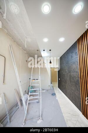 Renovation concept, new kitchen before renovation works and after, shiny tiles on the floor, modern chandeliers hanging from ceiling vs messy room with ladder in the middle Stock Photo