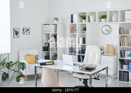 Office of business person with desk, armchair of professional, chair for clients, shelves, clock, green plant and two pictures on wall Stock Photo
