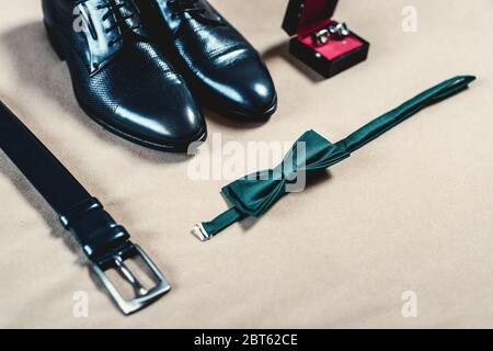 Closeup of elegant stylish black male accessories isolated on yellow fabric. High angle view of belt, shoes, cufflinks and green bow tie. Stock Photo