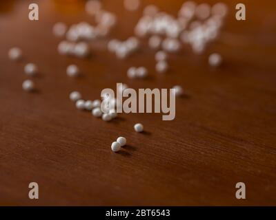 Homeopathic pills/globules spill on a wooden brown surface Stock Photo