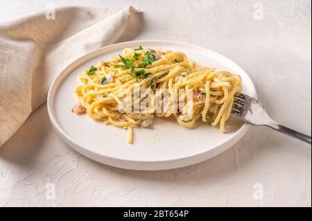 Classic homemade pasta carbonara Italian with bacon, eggs, parmesan cheese on light ceramic plate with fork and napkin on light table. Close up view Stock Photo