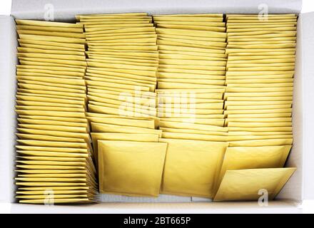 Lot of yellow paper postal envelopes in a shipping cardboard box. Top view, isolated on white. Stationery and office supplies. Stock Photo