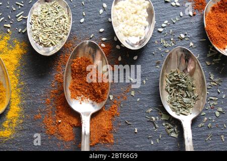 Flat lay photograph of teaspoons of various herbs, spices and seeds on a slate background.  Raw ingredients for cooking Stock Photo