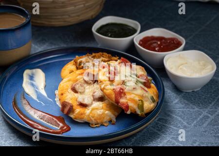 Assorted min pizza with tomato sauce, Green chutney and mayonnaise as side dish served on a blue plate and cup of hot tea Stock Photo