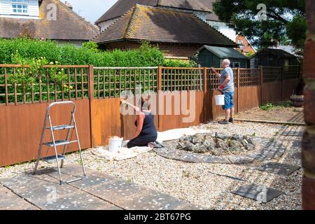 Ashford, Kent, UK. 23rd May, 2020. Friends and neighbours in the village of Hamstreet near Ashford in Kent occupy their time with chores about the house. This couple are busy at work painting the garden fence. ©Paul Lawrenson 2020, Photo Credit: Paul Lawrenson/Alamy Live News Stock Photo