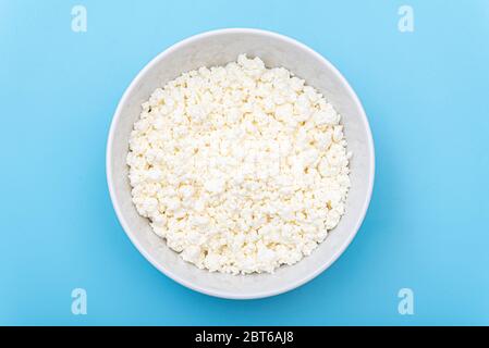 Fresh cottage cheese in a white bowl on a blue background. Milk curd on a plate. Top view. Stock Photo