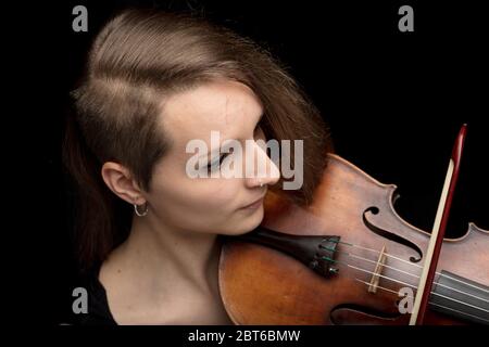 Young woman with modern haircut playing a classical violin during a performance against a dark background in a close up high angle view Stock Photo