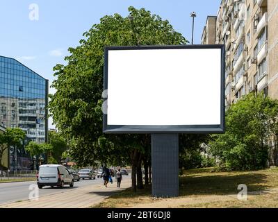 Empty banner on a city street with residential and office buildings and with green trees along the road. Blank billboard mockup with copy space. Stock Photo