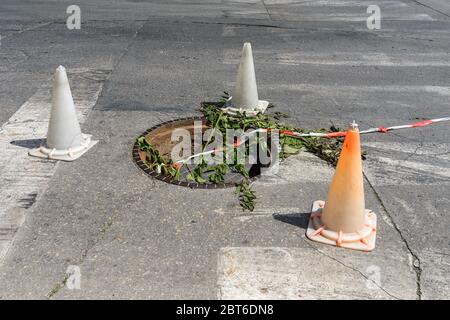 Open manhole marked with old traffic cones on a city street. Manhole with broken cover on a  narrow road. Dangerous traffic situation. City life. Stock Photo