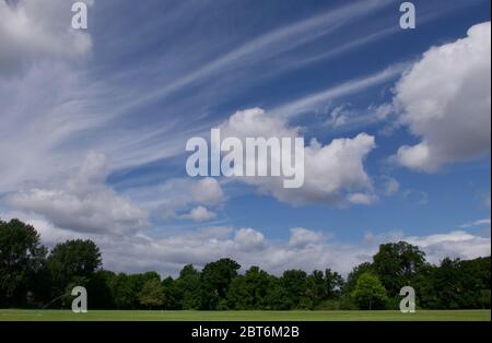 Unusual cloud formation in blue sky above trees and green field Stock Photo