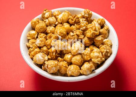 Plate with caramel popcorn on a red background Stock Photo